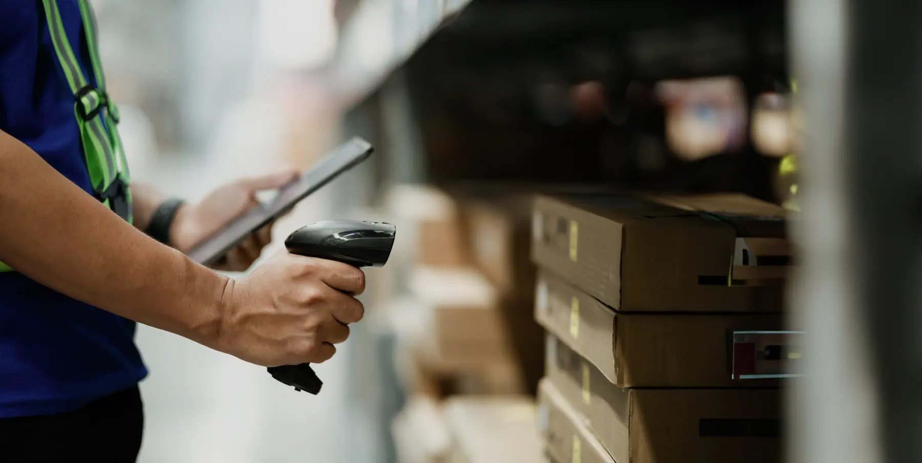 Hand mit Barcode-Scanner vor Kartons im Lager